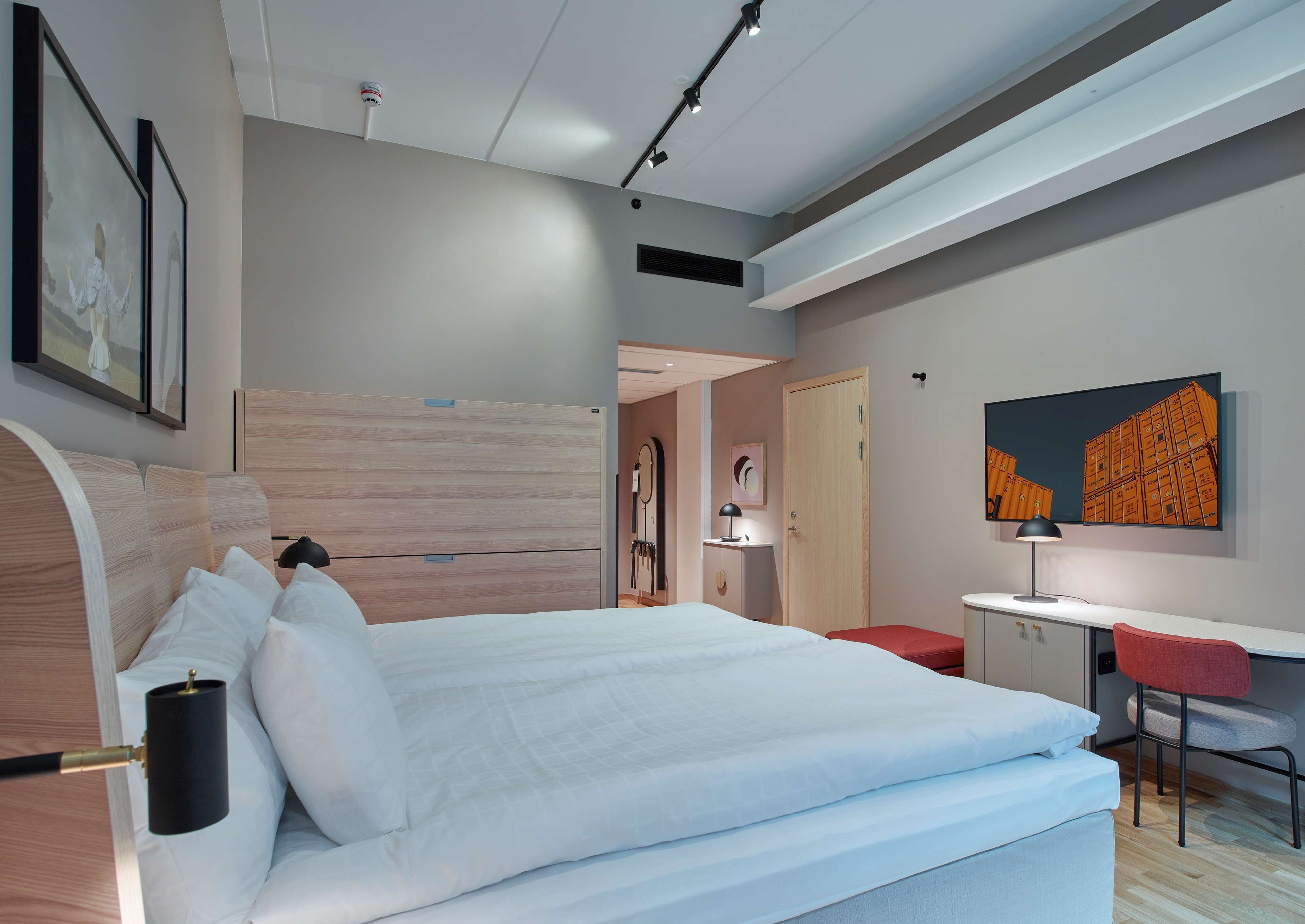 Een moderne hotelkamer met een groot bed, een bureau met stoel, een televisie en kunstwerken aan de muren.