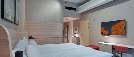 A modern hotel room with a large bed, a desk with a chair, a TV, and artwork on the walls.