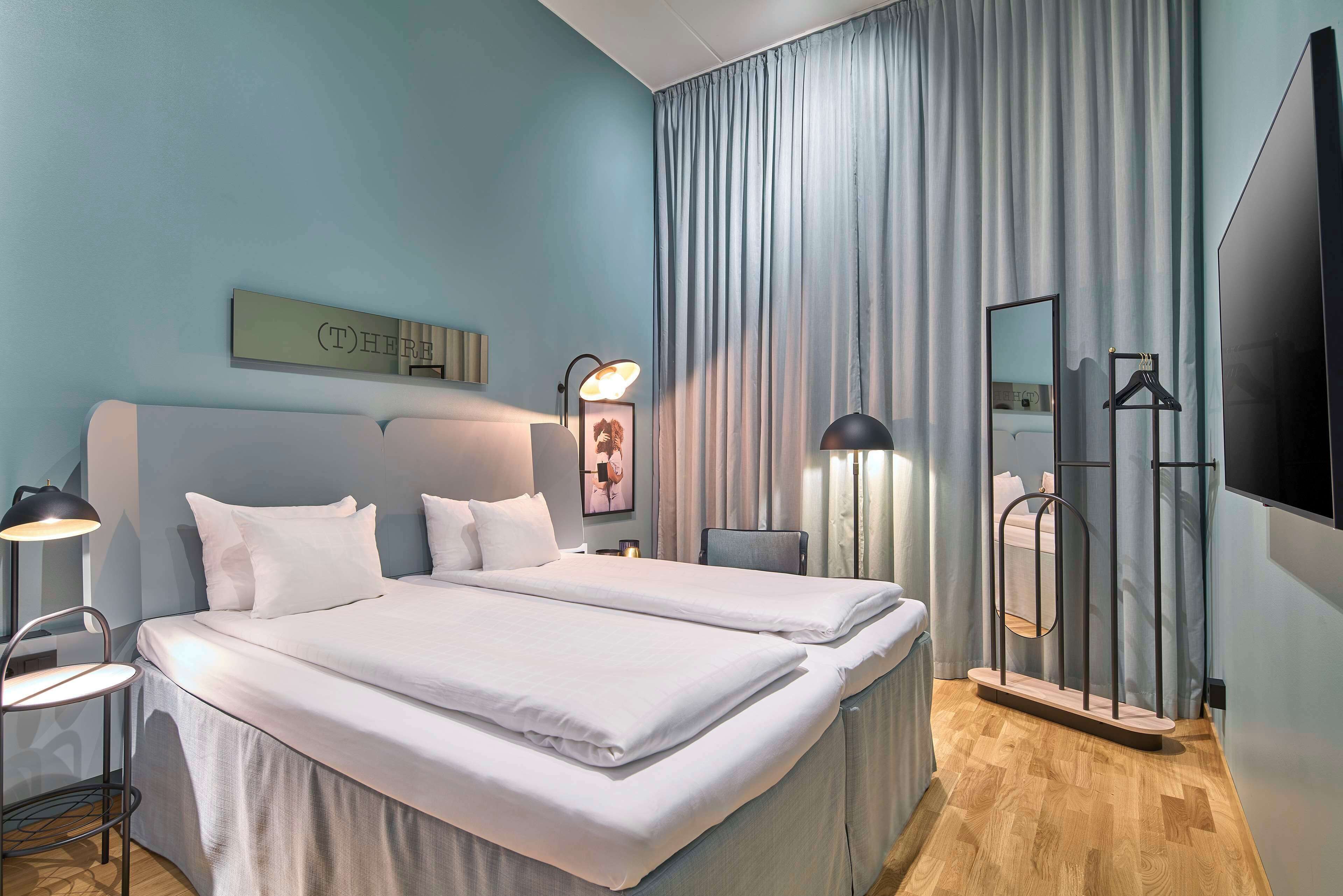 Ett modernt hotellrum med en stor säng, två sängbord, ett skrivbord, en stol, en platt-TV och en spegel.