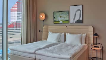 A hotel room with a large bed, a view of a building outside, and two framed artworks on the wall.