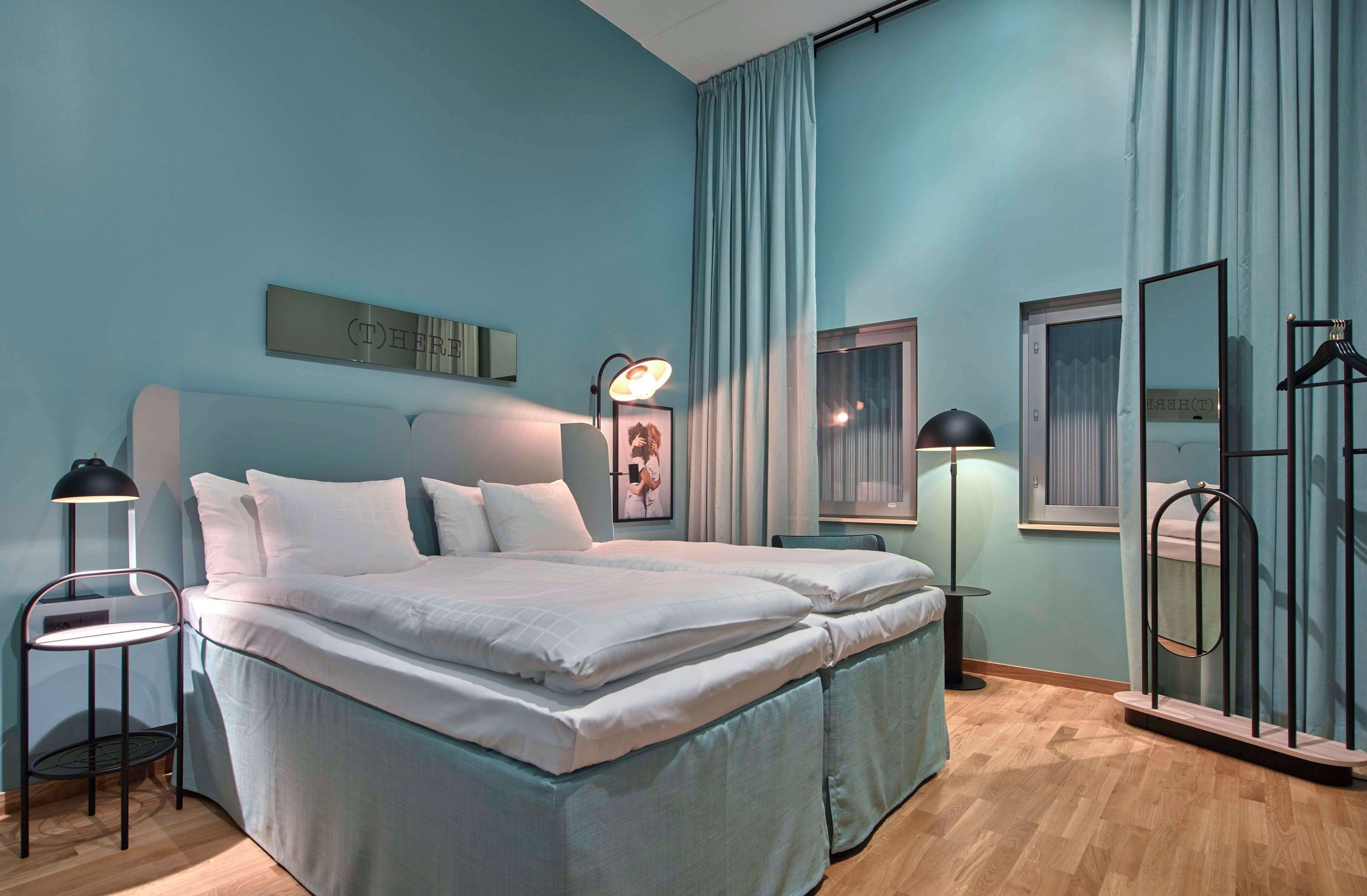 A bedroom with a bed, bedside tables, a mirror, and a window with curtains.
