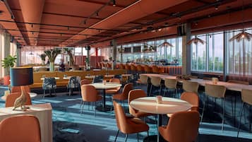 En rymlig restaurang med högt i tak, stora fönster och ett varierat utbud av sittplatser, inklusive bord och avskilda sittgrupper.