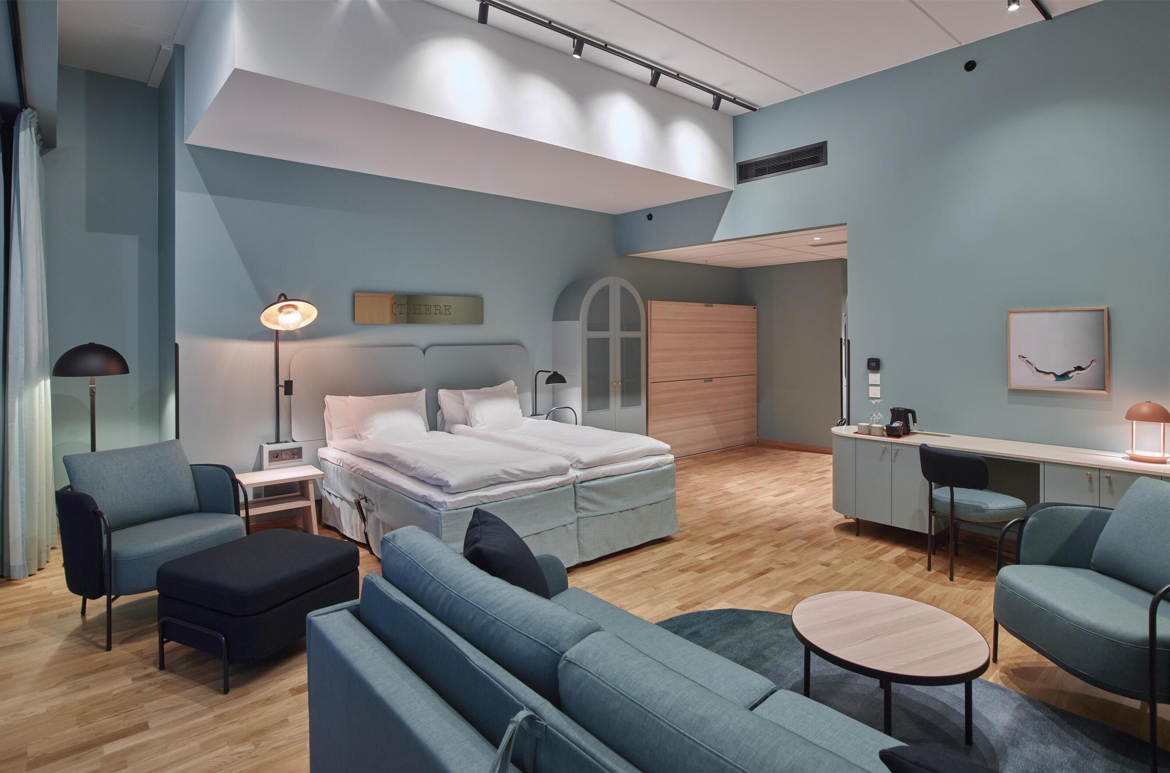 Un dormitorio moderno con cama, mesitas de noche, un escritorio y un área de descanso.