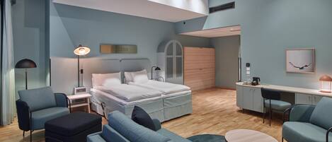 Un dormitorio moderno con cama, mesitas de noche, un escritorio y un área de descanso.