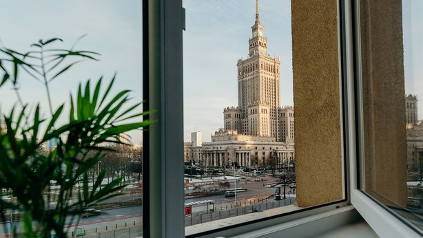 A view of a tall building with a spire, seen through a window with a beige curtain. - ShortStayPoland Panska (Warsaw)