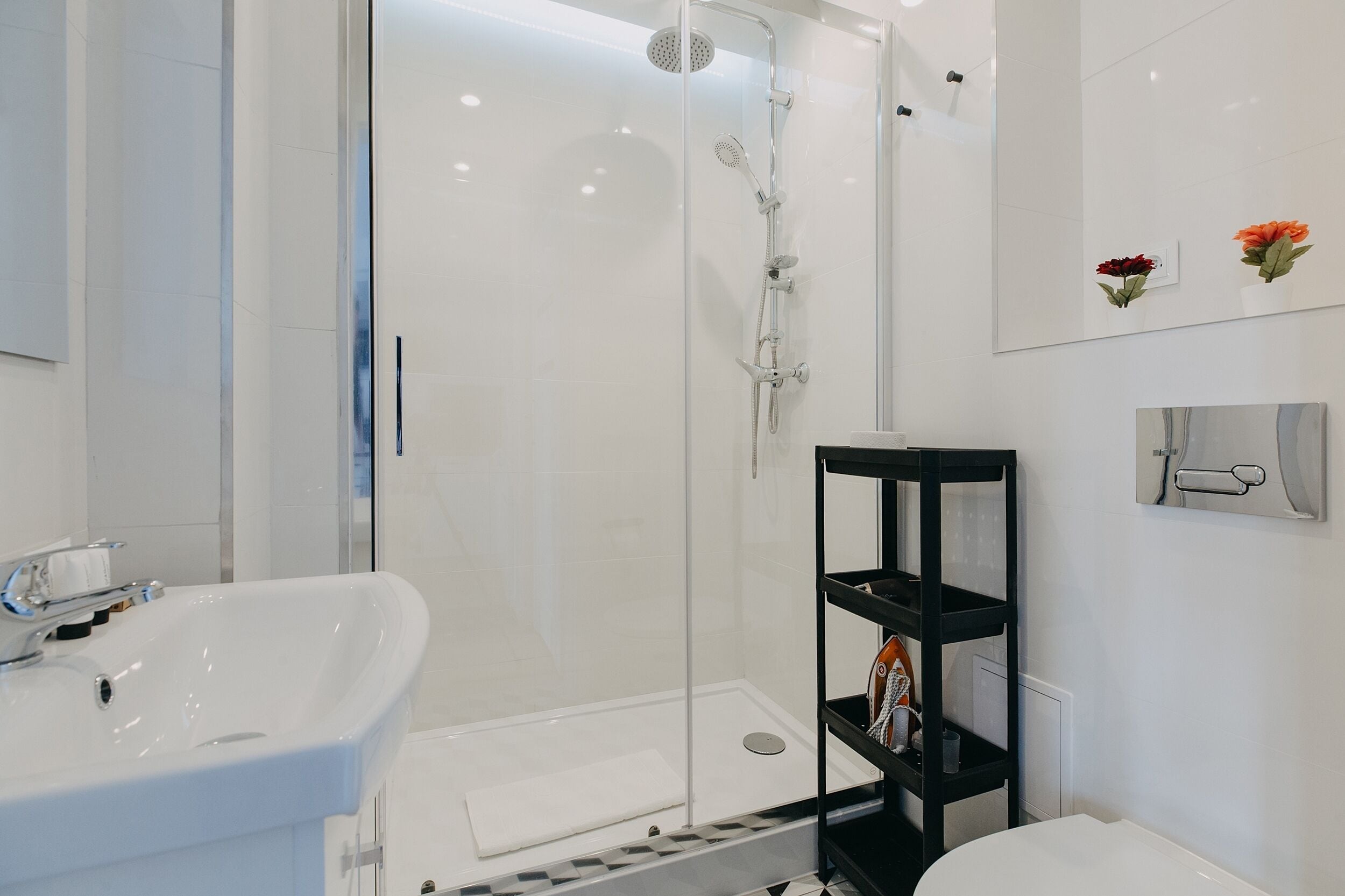 A modern bathroom with a glass-enclosed shower, a white sink, and a black shelf unit.