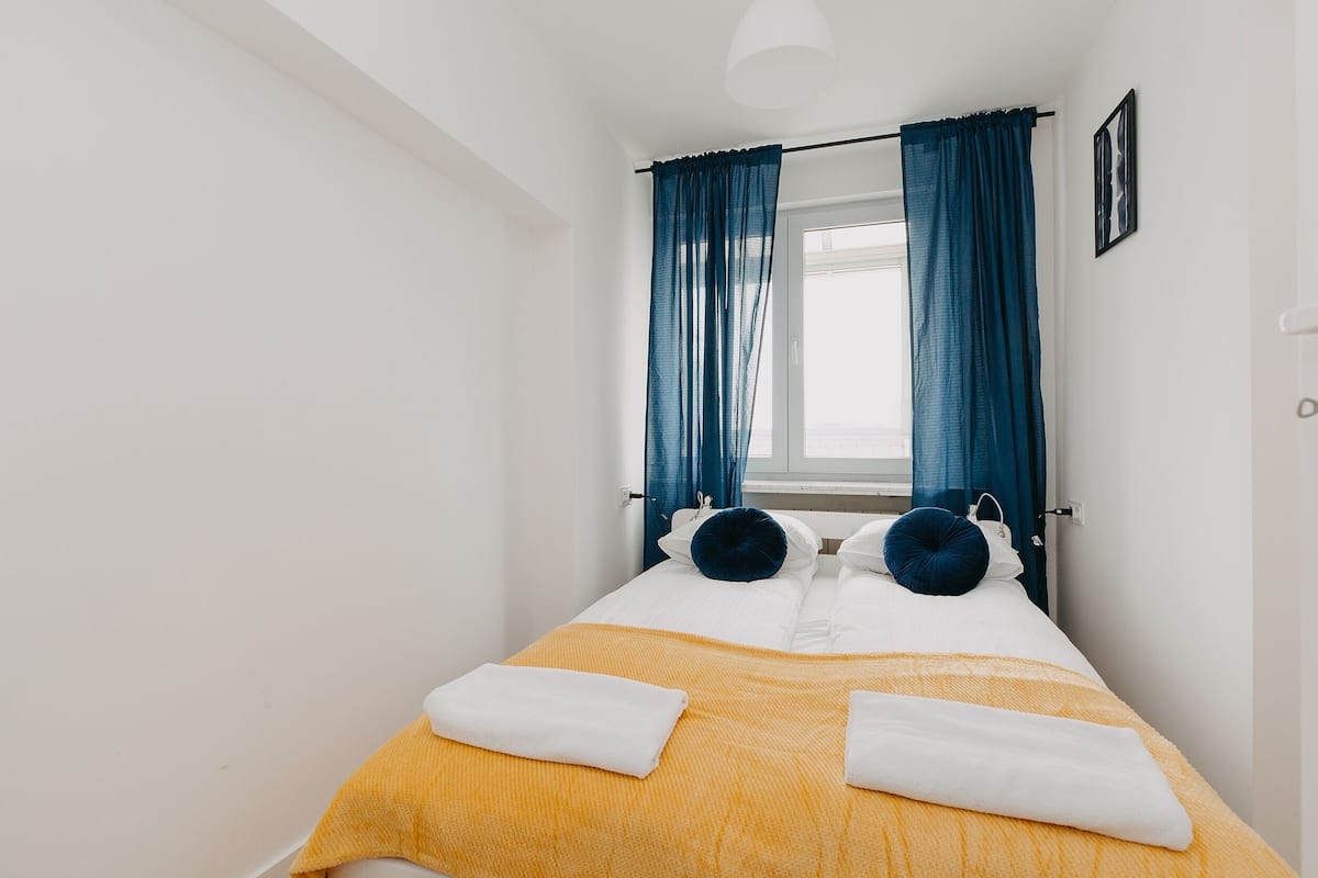 A single bed with a yellow bedspread, two pillows, and a white towel folded on the bed.
