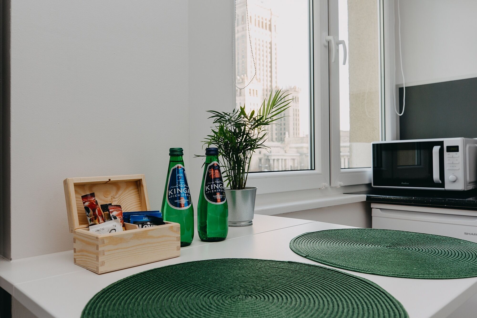 A kitchen with a microwave, wooden box, green bottles, and a potted plant.