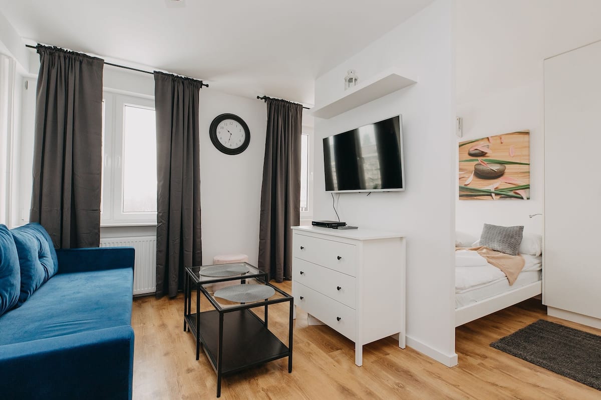 A modern bedroom with a bed, a TV, a desk, and a blue sofa.