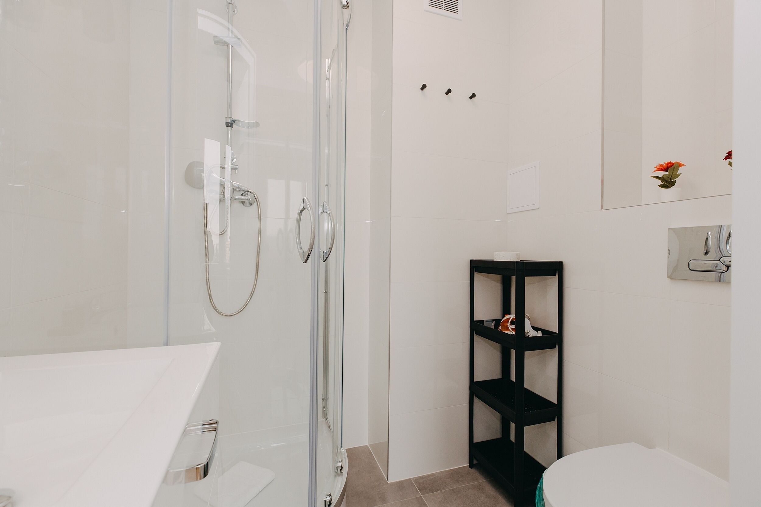 A modern bathroom with a glass-enclosed shower, a white sink, and a black shelf unit.