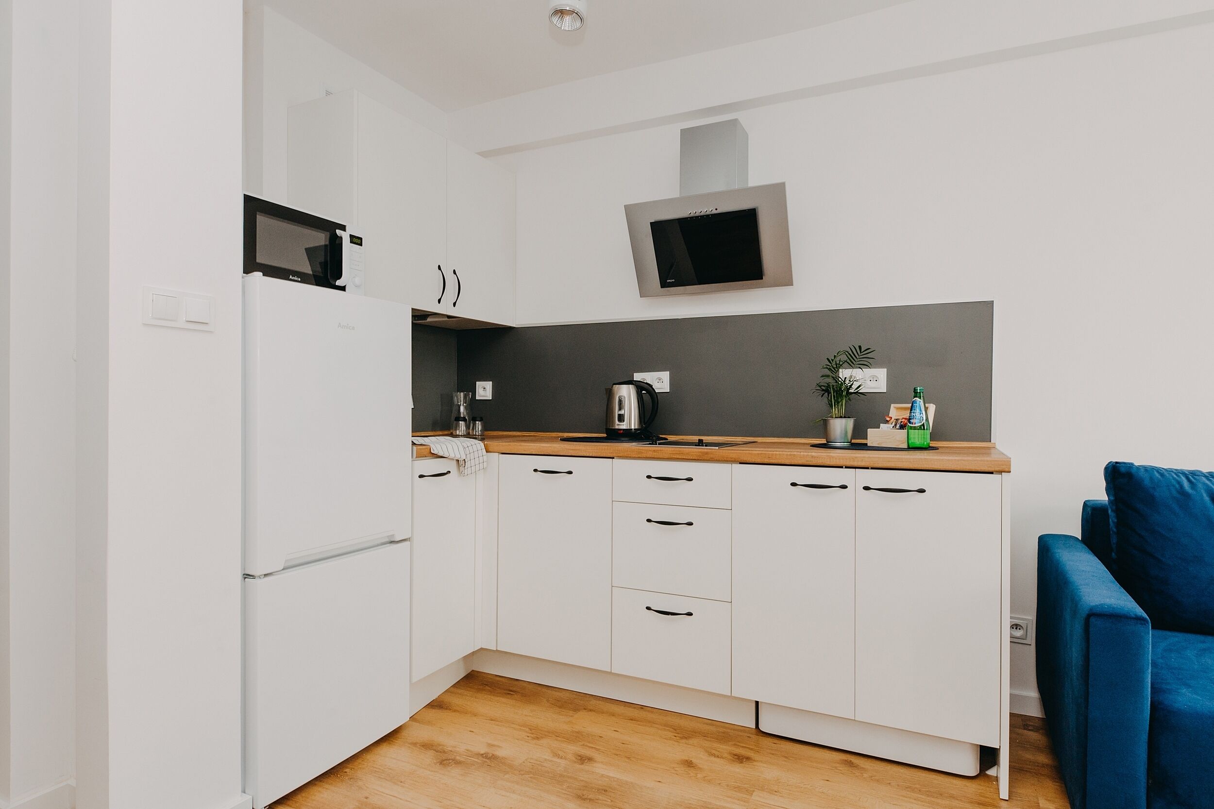 A compact kitchen with white cabinets, a microwave, a kettle, and a small sink.