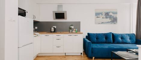 A compact kitchen with white cabinets, a microwave, and a kettle on the counter. There's a blue sofa and a small table with a tray.