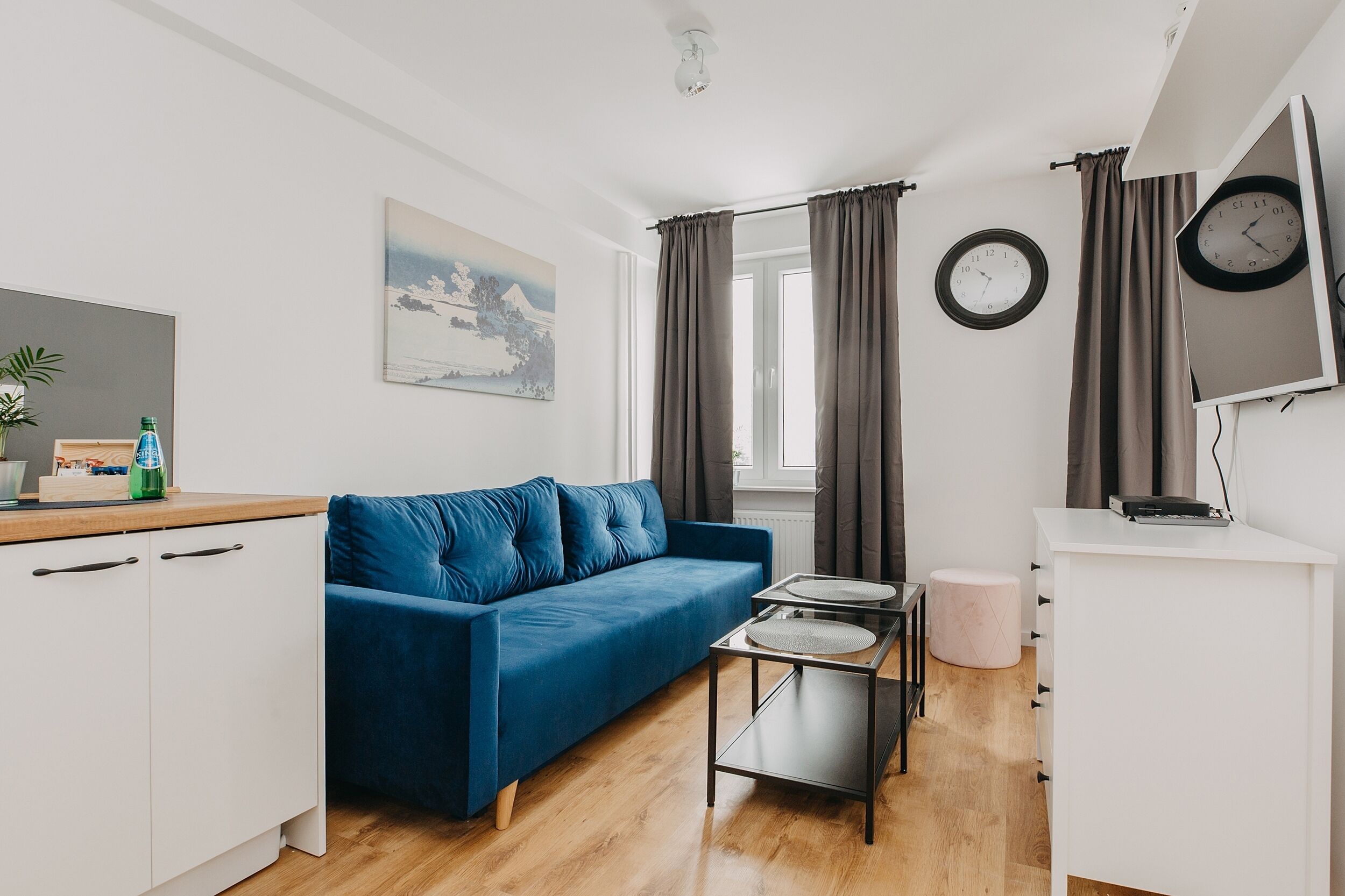 A modern living room with a blue sofa, a small coffee table, a white cabinet, and a painting on the wall.