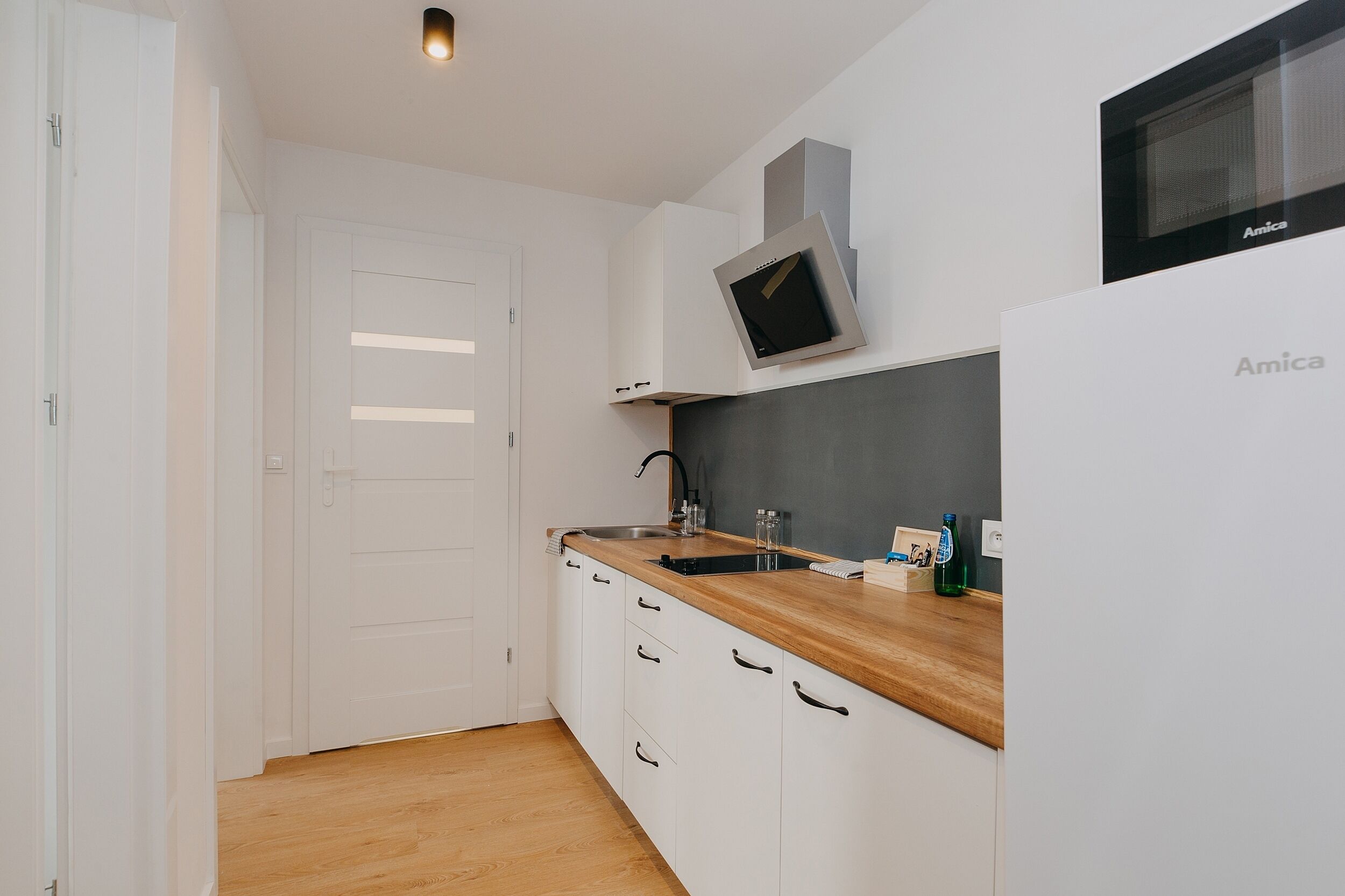A compact kitchen with white cabinets, a wooden countertop, a sink, and a microwave.