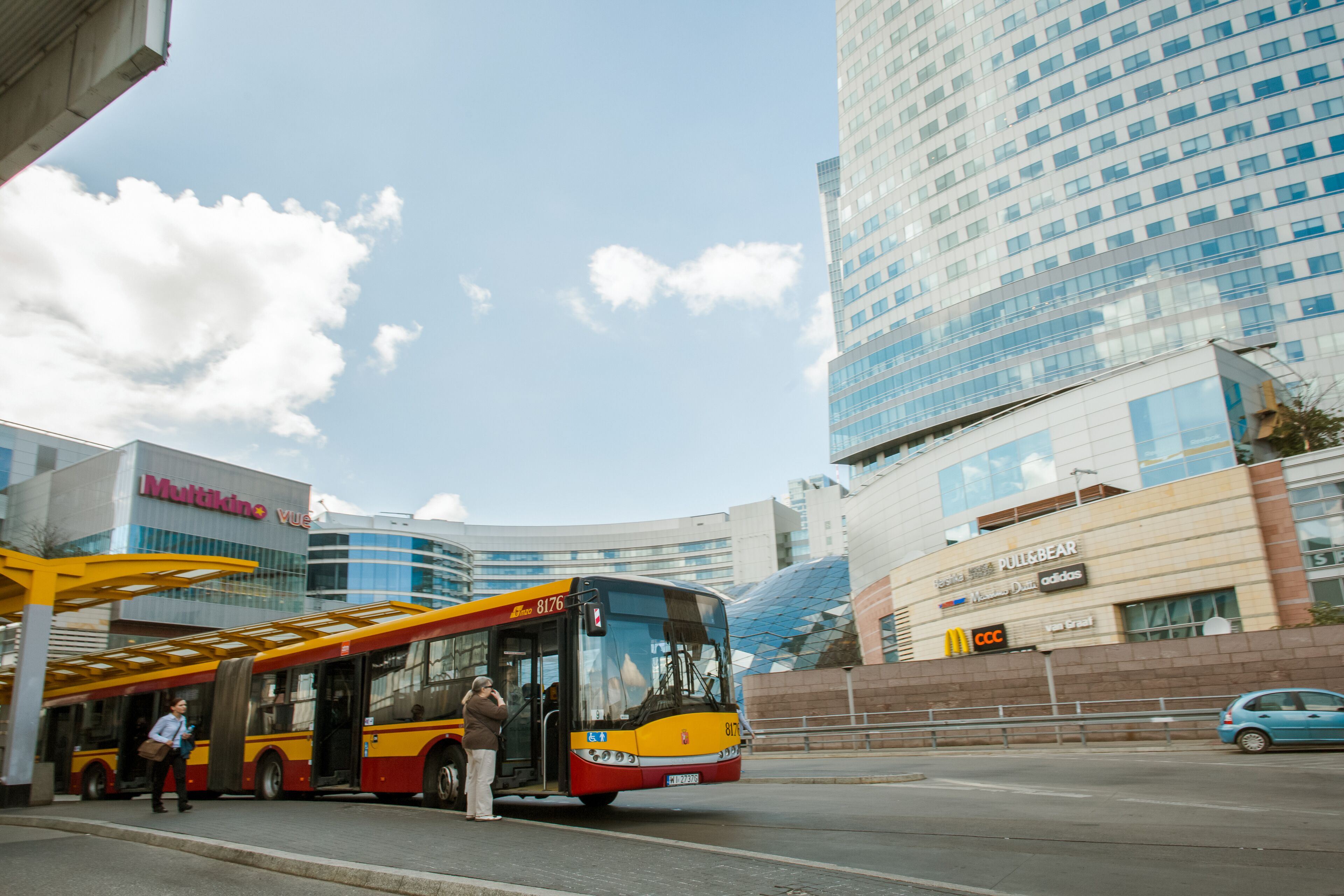 Un autobús en una parada de autobús, con un edificio moderno al fondo.