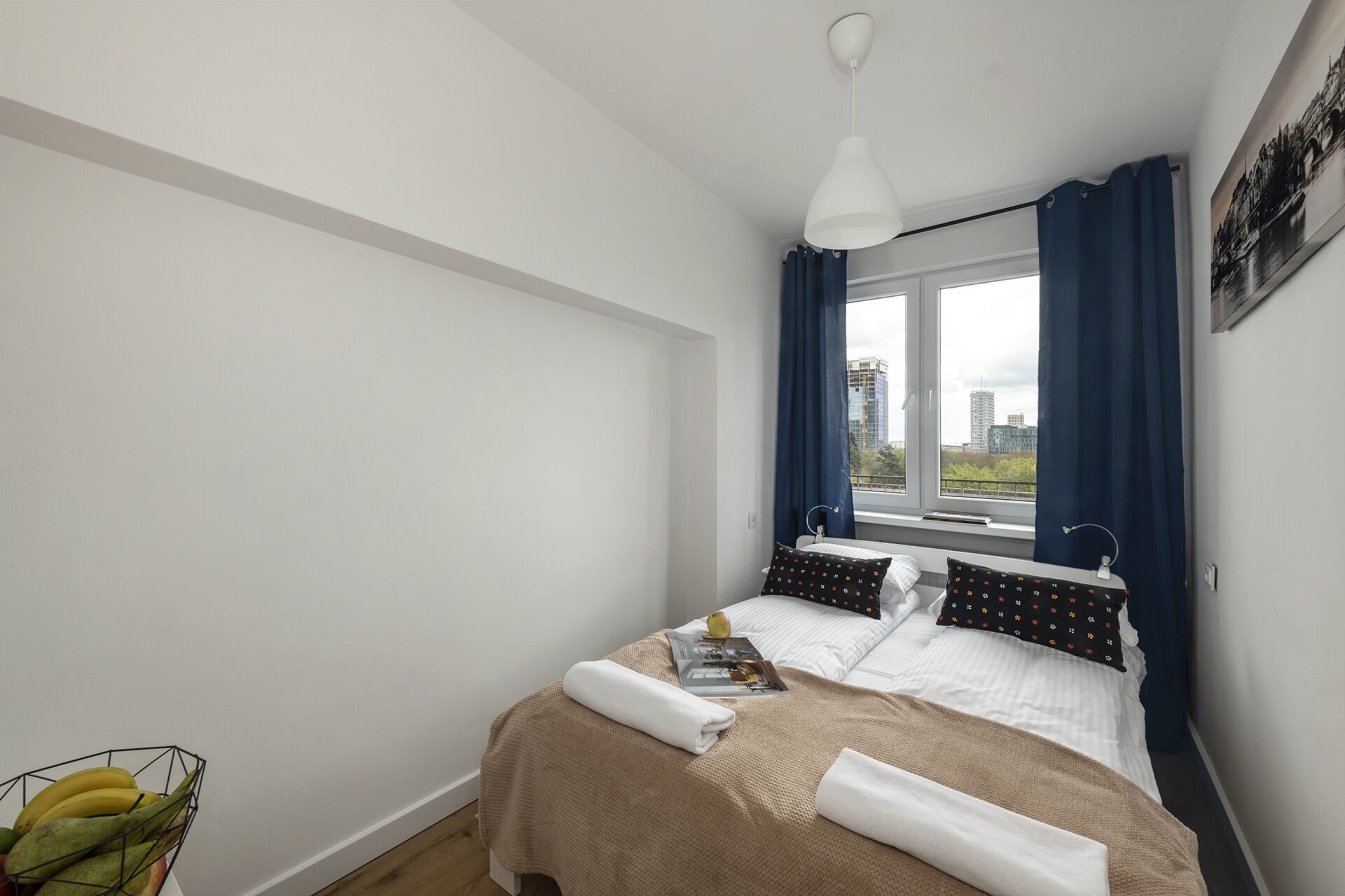 A bedroom with a bed, a window with curtains, a bedside table, and a wall-mounted picture.