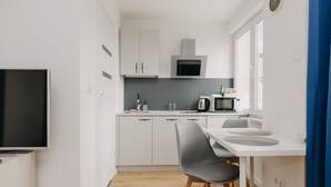 A modern kitchen with white cabinets, a microwave, a stove, and a dining area with a table and chairs. - ShortStayPoland Panska (Warsaw)