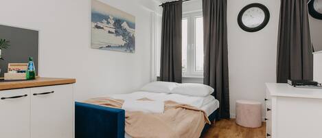 A bedroom with a bed, a desk, a chair, a small stool, a wall clock, and a painting.