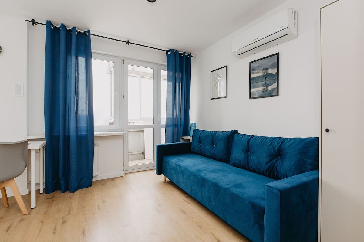A room with a blue sofa, a desk, and a window with blue curtains.