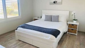 A bedroom with a bed, bedside tables, a window with blinds, a wall-mounted picture, and a potted plant. - Malua Bay Beach house (MALUA BAY)