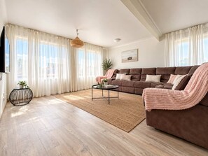 A modern living room with a brown sofa, a coffee table, and a large window with sheer curtains. - Malua Bay Beach House | Wake Up to the Waves (MALUA BAY)