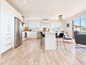 A modern kitchen with white cabinetry, stainless steel appliances, and a central island with bar stools.