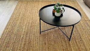 A round black table with a white vase and a plant on it, placed on a woven rug. - Malua Bay Beach house (MALUA BAY)