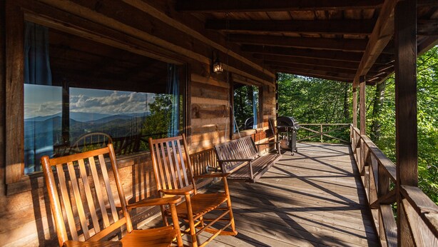 A wooden deck with a view of mountains through large windows.