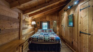 A log cabin bedroom with a bed, a window, a lamp, and a door.