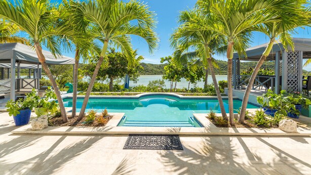 A pool area with palm trees, a view of the water, and a covered seating area. - Water front, with amazing elevated views, pool, flamingoes, private and quiet (Provienciales)
