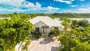 A white house with a sloped roof, surrounded by lush greenery and a clear blue sky. - Water front, with amazing elevated views, pool, flamingoes, private and quiet (Provienciales)