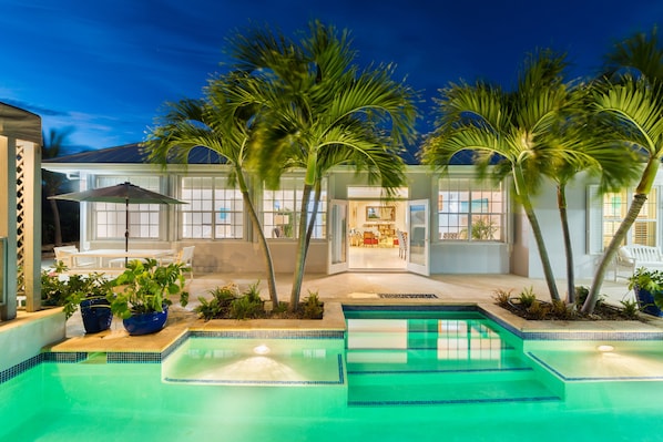 A swimming pool with a tiled border, surrounded by palm trees and potted plants.