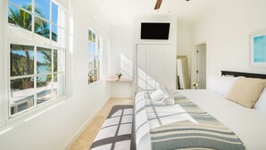 A hotel room with a bed, a ceiling fan, a TV, and large windows with a view of palm trees. - Water front, with amazing elevated views, pool, flamingoes, private and quiet (Provienciales)