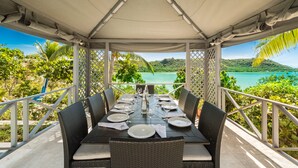 A covered dining area with a table set for six, overlooking a scenic view of a turquoise sea and lush greenery. - Water front, with amazing elevated views, pool, flamingoes, private and quiet (Provienciales)
