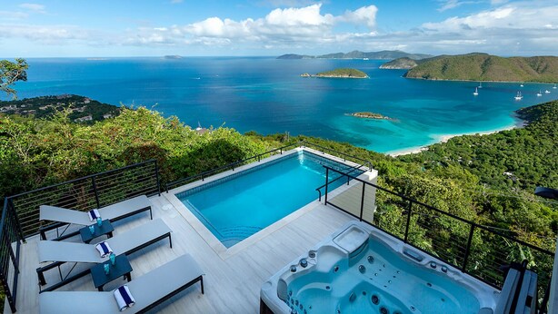 A rooftop infinity pool with a hot tub, lounge chairs, and a scenic ocean view.