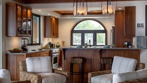 A modern kitchen with wooden cabinets, a central island, bar stools, and a large window.