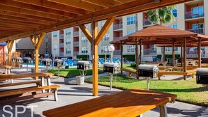 An outdoor patio area with wooden benches and barbecue grills, surrounded by a multi-story building with balconies.