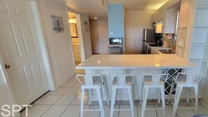 A modern kitchen with white cabinetry, a central island with bar stools, and a microwave above the island.