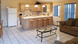 Une cuisine compacte dotée d’un îlot central, de tabourets en bois et d’une table à plateau en verre.