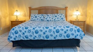 Un lit recouvert d’une couvre-lit à motifs bleus et blancs, flanqué de deux tables de chevet sur lesquelles sont posées des lampes, dans une pièce dont le sol est carrelé.