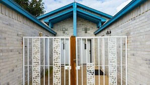 Une entrée fermée par un portail en métal blanc décoratif et un poteau en bois.