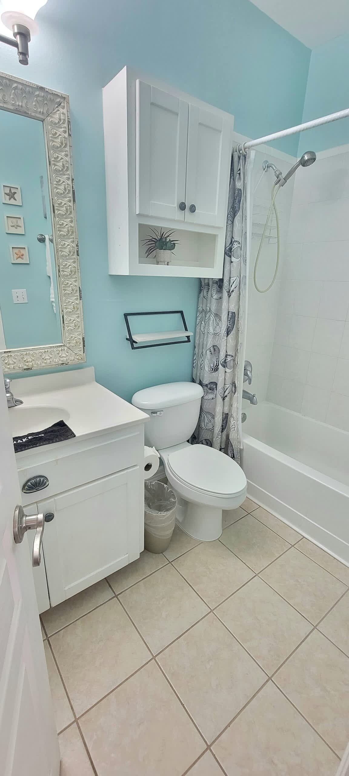 Un baño con inodoro, lavamanos y bañera. Hay una cortina de ducha con diseño floral.