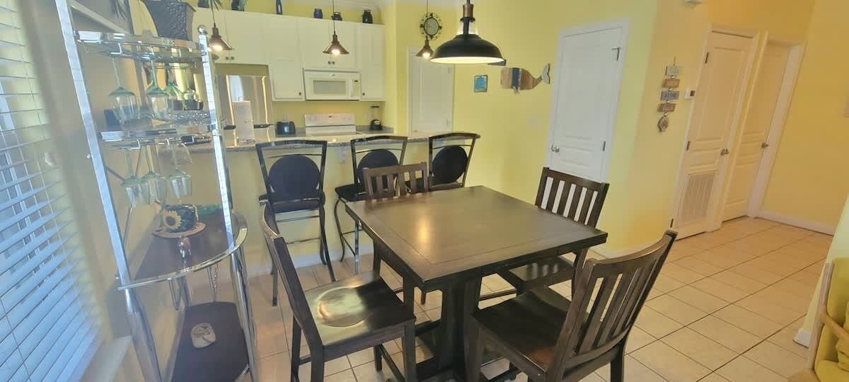 Un comedor con una mesa y sillas de madera, un estante de vidrio con utensilios de cocina y un microondas blanco al fondo.