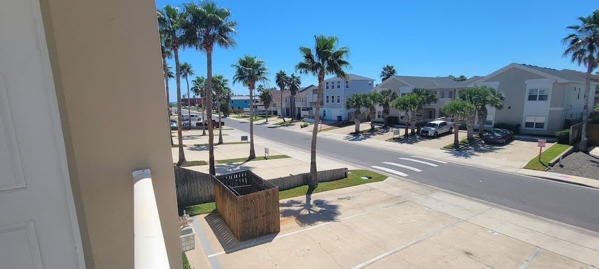 A residential street with palm trees, houses, and parked cars.