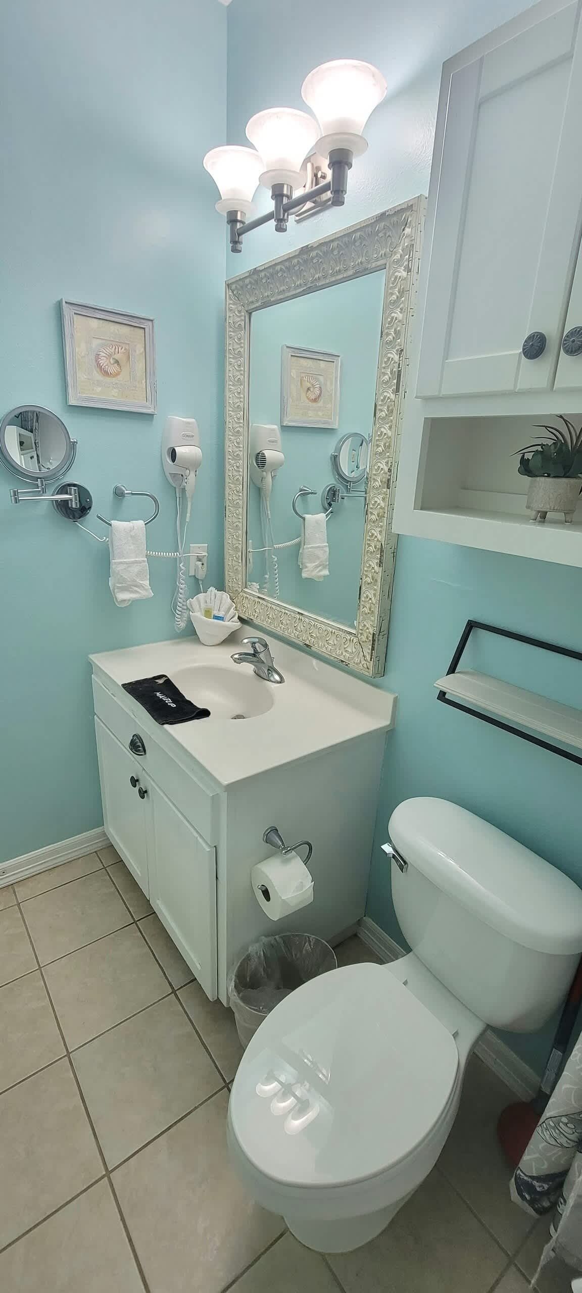A bathroom with a white sink, a mirror with a decorative frame, a toilet, and a trash bin.