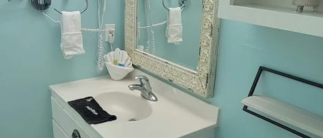 A bathroom with a white sink, a mirror with a decorative frame, a toilet, and a trash bin.
