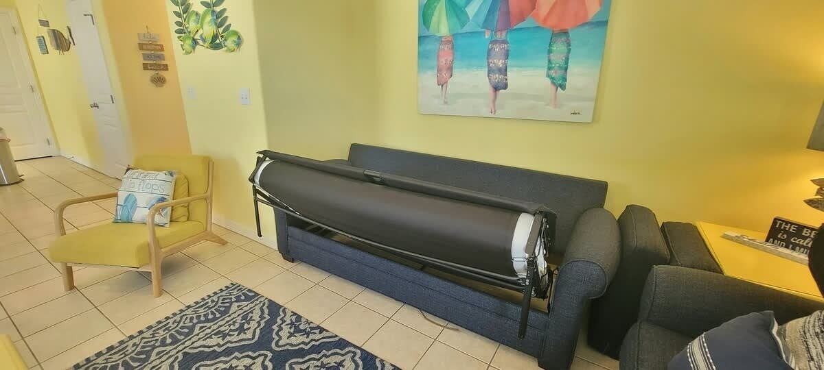 A living room with a sofa, a chair, a rug, and a painting on the wall.