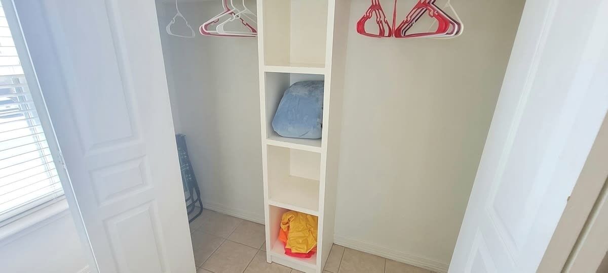 A closet with shelves and hanging space, a window, and a door.