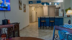 Een moderne keuken met een blauwe accentmuur, een eethoek met een televisie en een bar met twee krukken.