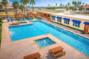 A swimming pool with lounge chairs, a small hot tub, and a covered seating area.
